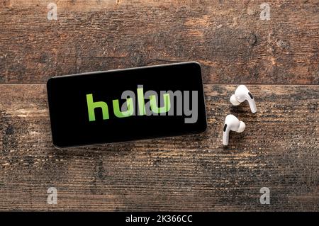 USA, NEW YORK 22. September 2022: Nahaufnahme des Telefons mit neuem Hulu-Logo und modernen Kopfhörern auf altem Holztisch. Hulu ist ein weltweit bekannter Anbieter von Stockfoto