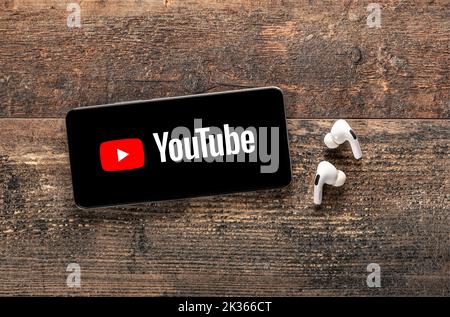 USA, NEW YORK 22. September 2022: Nahaufnahme des Telefons mit neuem Youtube-Logo und modernen Kopfhörern auf altem Holztisch. YouTube ist weltweit bekannt Stockfoto