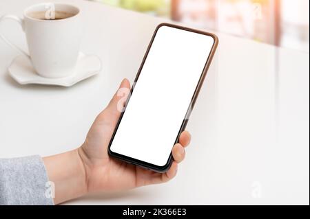 Modup-Telefon. Nahaufnahme Hand hält Handy Smartphone mit leerem Bildschirm im Café. Schwarzes Mobiltelefon mit weißem Bildschirm in weiblicher Hand Stockfoto