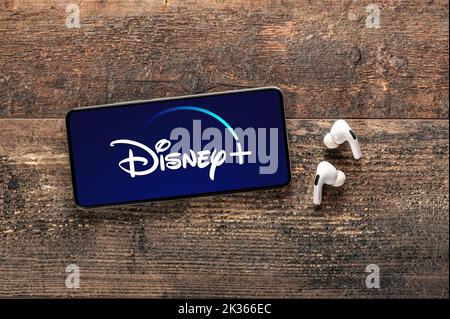 USA, NEW YORK 22. September 2022: Nahaufnahme des Telefons mit neuem Disney-Logo und modernen Kopfhörern auf altem Holztisch. Disney PLUS ist weltweit bekannt Stockfoto