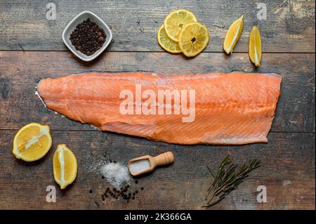 Fischfilet mit kulinarischen Zutaten, Kräutern, Salz, Pfeffer und Zitrone auf rustikalem Holztisch. Roher Forellenkadaver mit Gewürzen und Kräutern. Seefisch, gesund Stockfoto