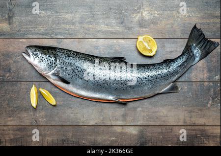 Geriebener Lachskadaver mit Zitrone liegt auf einem Holzbrett zum Schneiden von Fischen. Kadaver von atlantischem Lachs. Rohe Forellen Korpus auf Holztisch Hintergrund. Meer Stockfoto