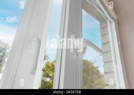 Offenes weißes Metall-Kunststoff-Fenster in der Wohnung gegen den blauen Himmel. Stockfoto