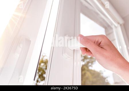 Eine Hand öffnet ein Fenster, um den Raum zu lüften. Einseitig geöffnetes Fenster. Stockfoto