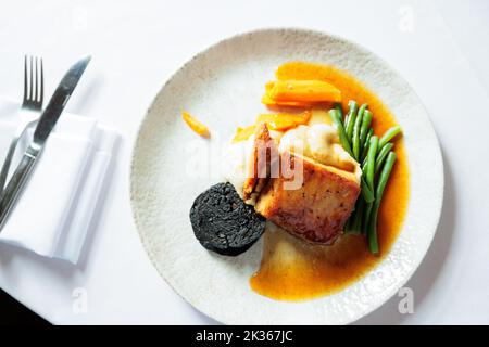 Langsam gebratenes Bauchschwein in einer Honig- und Sojaglasur mit schwarzem Pudding, Knistern und Salbei-Maische Stockfoto