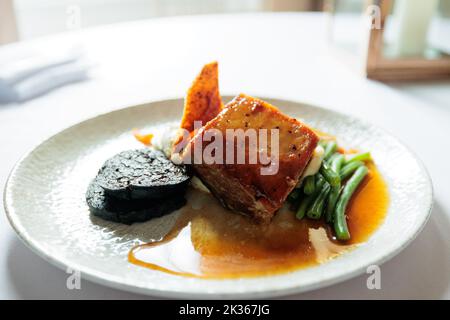 Langsam gebratenes Bauchschwein in einer Honig- und Sojaglasur mit schwarzem Pudding, Knistern und Salbei-Maische Stockfoto