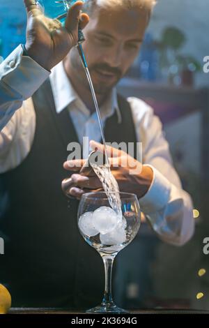 Professioneller Barkeeper in einem weißen Hemd und schwarzer Schürze, der bei einer Party im Nachtclub einen schönen Cocktail zubereitet. Nachtleben. Stockfoto