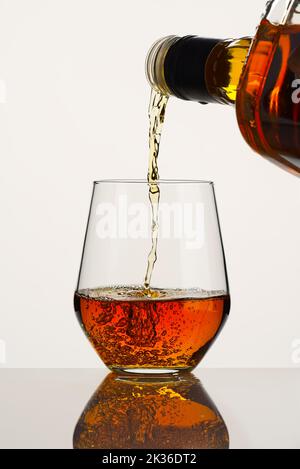 Whiskey oder Brandy, der aus einer Flasche auf weißem Hintergrund in ein Glas gegossen wird. Whisky aus einer Flasche gießen Stockfoto