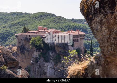 Östorthodoxes Heiliges Kloster von St. Varlaam vor dem Hintergrund von dicht bewaldeten Hügeln und Teil des benachbarten Felsens. Meteora, Griechenland Stockfoto