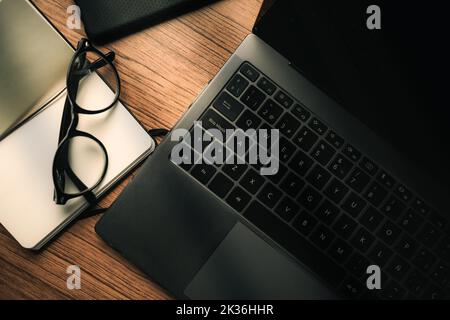 Ansicht des Vintage-Schreibtisches aus Holz mit Notebook, Notizblock, Smartphone und Brille von oben. Arbeitsplatz. Arbeiten Sie von zu Hause aus. Schreibtisch. Stockfoto