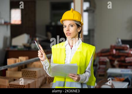 Eine Architektin gibt den Arbeitern auf der Baustelle in Innenräumen Anweisungen Stockfoto