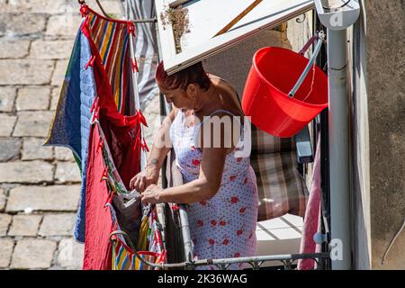 Eine italienische Dame mit roten Haaren hängt ihre Wäsche zum Trocknen in der Stadt Ragusa auf Sizilien, Italien Stockfoto