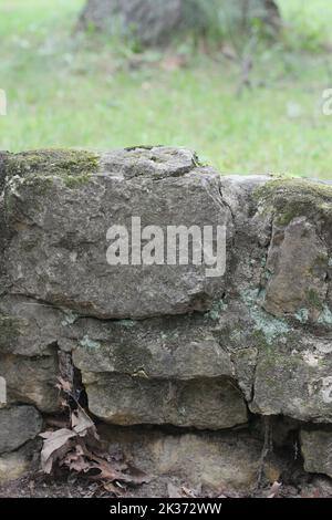 Ein alter verwitterter Steinzaun, der aus den Jahren des Gebrauchs zerbröckelt. Stockfoto