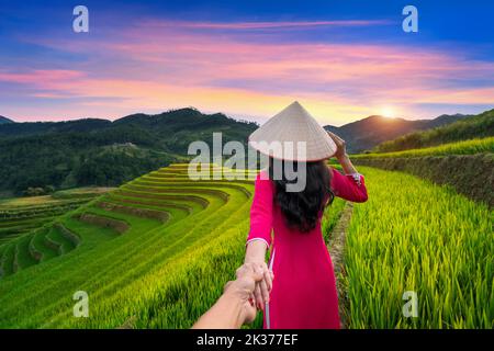 Asiatische Frau, die traditionelle vietnamesische Kultur trägt, hält die Hand des Mannes und führt ihn zu Reisterrassen in Mu Cang Chai, Yen Bai, Vietnam. Stockfoto