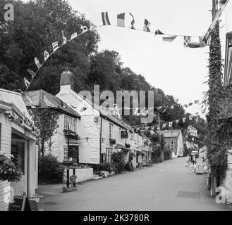 Schwarz-weiß image Bunting fliegt trotzig im Wind, aber das kornische Dorf Polperro sieht traurig und verlassen in der späten Saison September Stockfoto