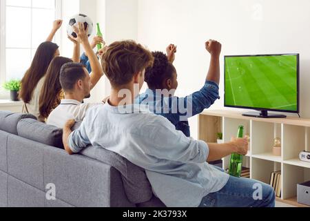 Eine Gruppe von Freunden sitzt auf dem Sofa, trinkt Bier und schaut sich ein Fußballspiel im Fernsehen an Stockfoto