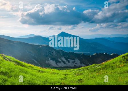 Idyllische Frühlingslandschaft in den Alpen mit frischer grüner Wiese und Berggipfeln im Hintergrund. Morgen alpines Hochland in sonnigen Tag. Wunderschöne Naturlandschaft. Beliebtes Touristenziel Stockfoto