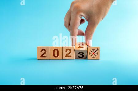 Das Kalenderjahr 2022 wurde mit dem Ziel und dem erfolgreichen Konzept auf 2023 geändert. Handdrehende Holzwürfelblöcke für den Übergang von 2022 auf 2023 mit Stockfoto