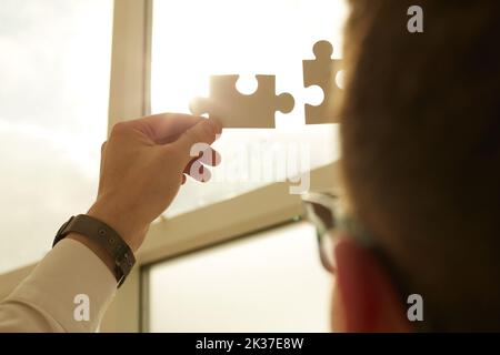 Geschäftsmann händen Puzzleteile, die die Fusion zweier Unternehmen oder eines Joint Ventures, einer Partnerschaft, einer Fusion und eines Akquisitionskonzepts darstellen. Stockfoto