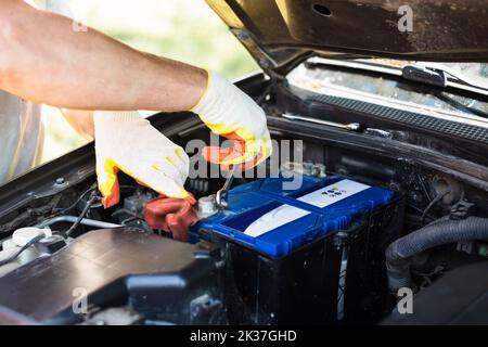 Austauschen der Batterie in einem Auto. Der Mechaniker schraubt die Batteriebefestigungen mit einem Schraubendreher ab. Stockfoto