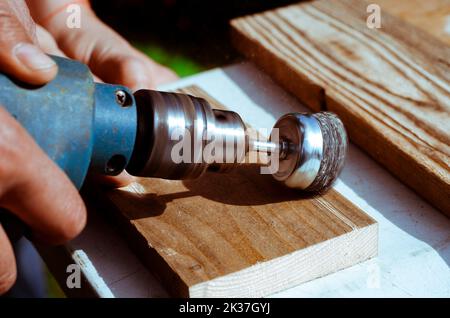 Hände Mann mit elektrisch rotierender Bürste Metallscheibe Schleifen ein Stück Holz. Holzbearbeitung im Freien. Stockfoto