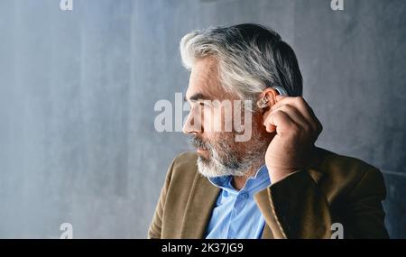 Grauhaariger reifer Mann mit Hörbehinderung, der Hörgeräte verwendet. Hörlösungen für Gehörlosigkeit Menschen Stockfoto