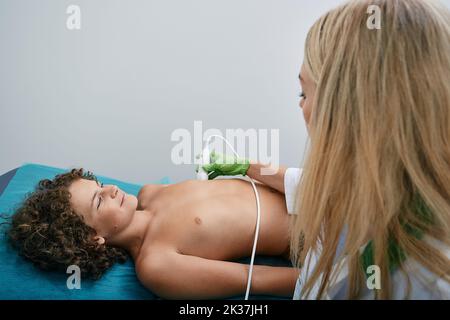 Junge Patientin, die mit Elektrokardiogramm-Geräten die Herzgesundheit überwacht, mit einer Kardiologin. Kardiogramm-Test für Kinder Stockfoto