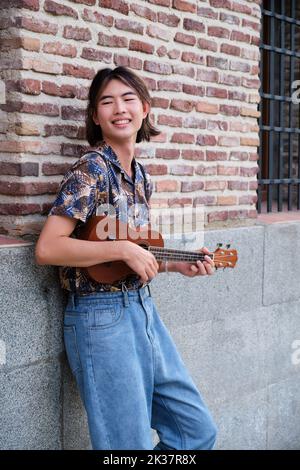 Taiwanese lächelt und spielt akustische Ukulele-Gitarre. Stockfoto