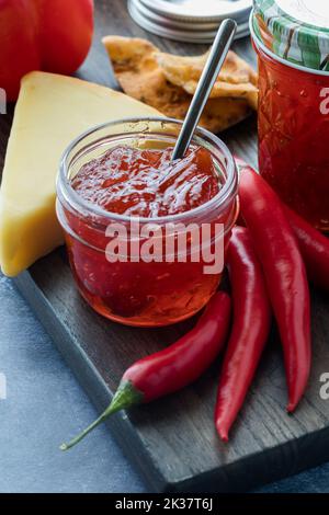 Ein Glas Peperoni-Gelee, umgeben von Paprika, Käse und Crackern. Stockfoto