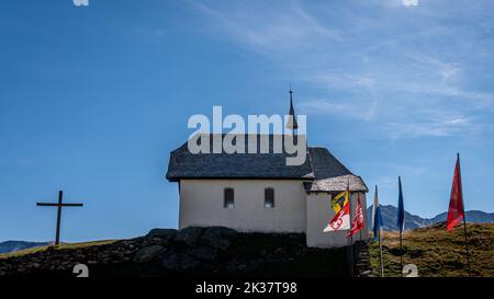 Landschaft aus Kirche und Bergen. Schweizer Bettmeralp-Kirche mit Schweizer Kantonsflaggen. Ruhige Szene. Stockfoto