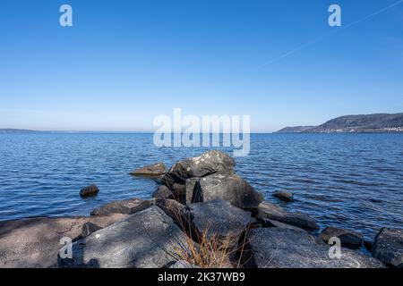 Felsbrocken als Teil eines Wellenbrechers in einem See. Bild vom See Vattern, Schweden. Blaues Wasser und Himmel im Hintergrund Stockfoto