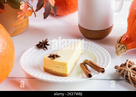 Kürbiskuchenstück auf weißem Teller, umgeben von reifen orangefarbenen Kürbissen, Herbstblättern und Tasse. Herbst oder Halloween oder Danksagekomposition. Fallen Sie holid Stockfoto