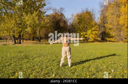 Eine junge Frau in einem Herbstpark genießt die Freiheit. Sie springt und gestikuliert weit. Stockfoto