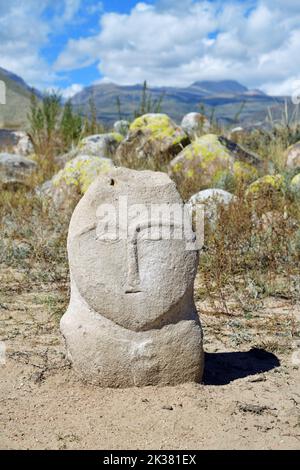 Eine alte turkische Steinstatue, die einen Mann gegen Berge darstellt. VII-X cc. AD. Cholpon ATA Petroglyphen, Issyk Kul, Kirgisistan Stockfoto