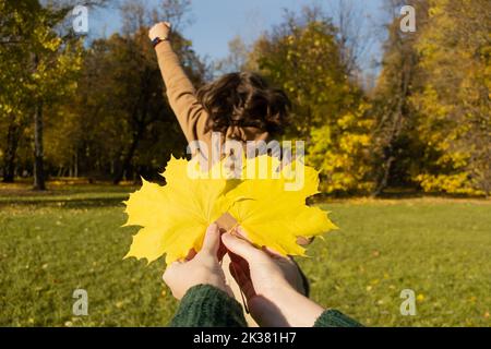 Nahaufnahme Handflächen mit gelben Ahornblättern wie Flügel auf dem Hintergrund der Frau von hinten, Hände hoch. Stockfoto