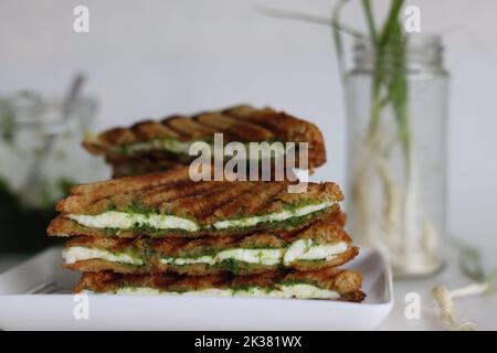 Chutney-Sandwich mit Käse. Gegrillte Sandwiches mit Quark-Scheiben und Gewürzen mit grünem Knoblauch. Chutney-Sandwich mit Käse. Aufgenommen auf weißem Hintergrund Stockfoto