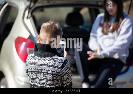 Ein kleiner Junge fotografiert ein Mädchen auf einem Smartphone. Stockfoto