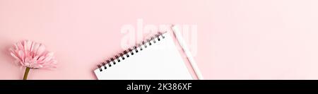 Notizbuch und Stift, Blume auf rosa Hintergrund. Copy Space Draufsicht Banner. Frau Arbeitsplatz, Geschäft, Studium, Freiberufler und Home-Office-Konzept. Stockfoto
