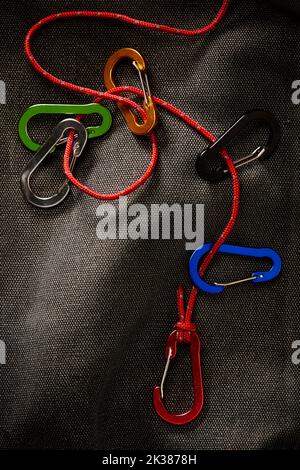 Farbenfrohe Karabiner-Accessoires an einem kleinen roten Seil mit dramatischer, dezenter Beleuchtung. Dieses Tool ist nicht zum Klettern, sondern in der Regel für Schlüsselanhänger oder Zugang Stockfoto