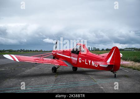 Ein roter Segelflieger schleppt auf der Startbahn des Rufforth Airfield, York, mit einem Schleppseil, das dahinter liegt, um einen Segelflieger in die Luft zu schleppen. Stockfoto