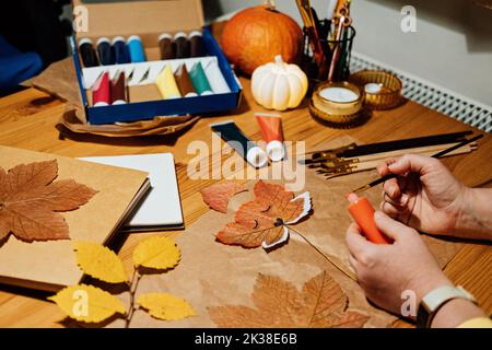 Herbsthandwerk aus getrockneten Blättern. DIY Herbst Crafts für Erwachsene. Collage aus Herbstnatur. Weibliche Hände zeichnen Fuchsgesicht auf trockenem Ahornblatt Stockfoto