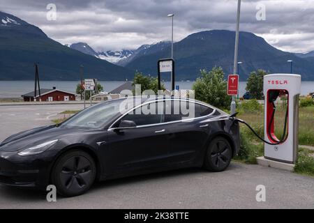 Skibotn, Norwegen - 25. Juli 2022: Eine statische Aufnahme eines soliden schwarzen Tesla Model 3 Dual Motor, der an einem bewölkten Sommertag am Skibotn Supercharger aufgeladen wird. Stockfoto