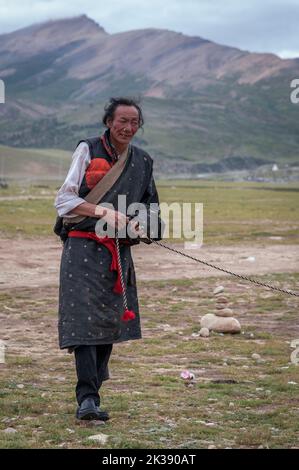 Tibetischer Pilger und ein Yak mit farbenfrohem und ethnischem Sattel an einer Aussichtsplattform östlich des Nyenchen Tanglha-Gebirges in Damxung, Lhasa, Tibet. Stockfoto