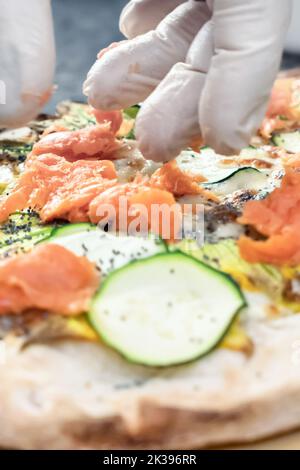 Pizza Art. Der Prozess der Herstellung von Pizza. Hände des Küchenchefs mit weißen Handschuhen, die Pizza machen. Nahaufnahme. Stockfoto