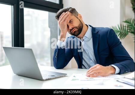 Gestresst besorgt verärgert müde kaukasischen Geschäftsmann, Corporate Director, Finanzmanager, sitzt im Büro am Arbeitsplatz, nervös der Frist ein Projekt, schloss seine Augen, Hand am Kopf haltend Stockfoto