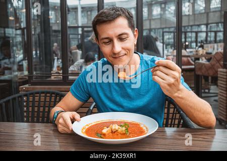 Mann, der köstliche Tomatensuppe im Café oder Restaurant isst. Vegetarische Küche und gesunde Gemüsediät. Abendessen und Mahlzeit mit Bio-Produkten Stockfoto