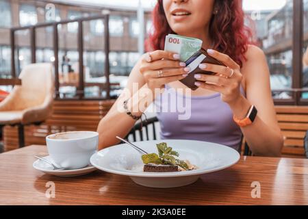 Das Mädchen wird für das Dessert in einem Café bezahlen und hat eine Geldbörse mit Euro-Banknoten herausgenommen. Preiserhöhung und Konzept für Inflation und Trinkgeld Stockfoto