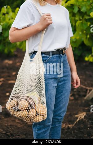 Verkürzte Ansicht eines Mädchens, das in einer umweltfreundlichen wiederverwendbaren Netztasche Schultergemüse aufsetzt. Zero Waste Konzept. Konzept der Umweltverschmutzung Stockfoto