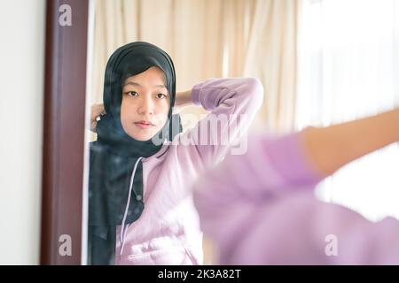 Spiegelung auf einem Wandspiegel einer muslimischen Frau, die ihren Kopftuch trägt. Stockfoto