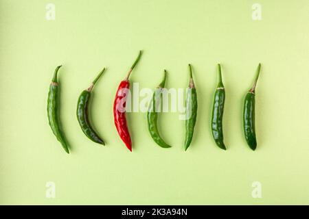 Grüne und rote Chilis auf körnigen strukturierten hellgrünen Hintergrund angeordnet, reifen und unreifen gemeinsamen Gemüse für ihren würzigen Geschmack verwendet Stockfoto